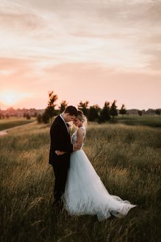 a bride and groom standing in tall grass at sunset