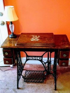 an old sewing table with a lamp on it in front of a wall painted orange