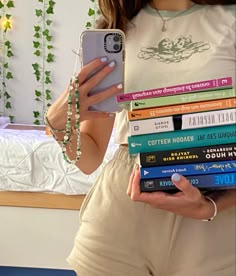 a woman holding a stack of books while looking at her cell phone and taking a selfie