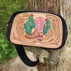 This bag has a hand-tooled leather patch featuring western floral carving and a cowgirl boot surrounded by cacti. It can be worn crossbody or around the waist. There is a large zippered opening and a small zippered pocket on the back. Western Style Crossbody Shoulder Bag For Travel, Western Hand Tooled Travel Bag, Western Style Hand Tooled Shoulder Bag For Travel, Western Style Hand-tooled Travel Bag, Western Style Hand-tooled Bags For Everyday Use, Western Style Crossbody Bags For Western-themed Events, Western Leather Bags With Concho Details, Western Saddle Bag For Everyday Use, Western Style Saddle Bags For Everyday Use