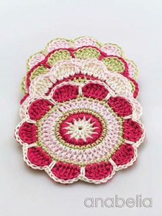 three crocheted coasters sitting on top of each other in pink, green and white