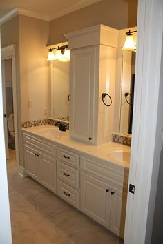 a large bathroom with two sinks and cabinets in it's center area, along with an open door leading to another room