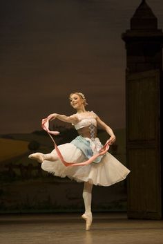 a young ballerina is performing with a ribbon in her hand and wearing a tutu