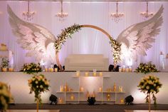 an altar decorated with angel wings and flowers, surrounded by candles in front of the altar