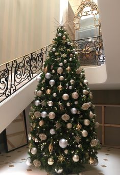 a decorated christmas tree sitting in the middle of a room next to a stair case