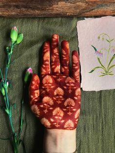 a person's hand with red and white designs on it next to some flowers