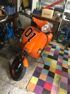 an orange scooter sitting on top of a checkered floor in a garage