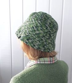 a woman wearing a green sweater and hat looking at a white boarderboard wall