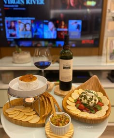 a table topped with plates of food next to a bottle of wine and a flat screen tv