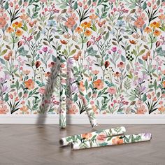 two rolls of wrapping paper sitting on the floor in front of a floral wallpaper