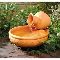 an orange water fountain in the middle of some plants