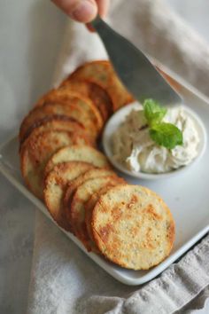 a person is cutting up some crackers on a white plate with a small bowl of whipped cream