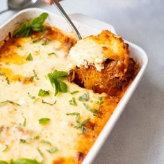 a casserole dish with meat and cheese being scooped from the casserole