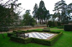 a checkerboard chess board in the middle of a garden with hedges and trees