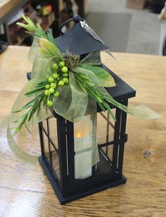 a small lantern with some green flowers on the front and one candle in the back