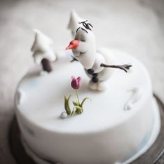 there is a cake decorated with frosting and flowers on the top, as well as an image of a snowman