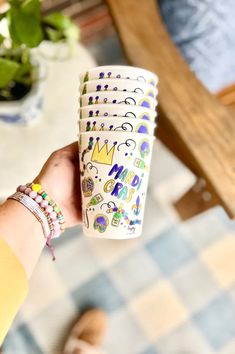 a hand holding a stack of six cups with designs on the outside and inside, in front of a table