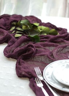 the table is set with white plates and silverware, along with purple linens