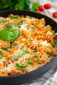 a skillet filled with pasta, cheese and greens on top of a table cloth