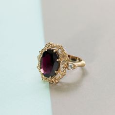 Elegant statement vintage style ring in 14k yellow gold, garnet and white cubic zirconia halo engagement, wedding or promise ring for women.   This impressive handmade ring is made of solid 14k yellow gold and is set with a big faceted oval red garnet, in a vintage style setting. Two smaller round white cz gems are set in a marquise setting, one on each side. The deep color of the gemstones combined with the unique design give this ring a bling chic that cannot be ignored.   Garnet is January's Gold And Garnet Ring, Antique Ruby Ring Gold, Ruby Engagement Ring Gold Vintage, Vintage Gemstone Ring, Ruby Red Engagement Ring, Garnet Engagement Ring Vintage, Colored Engagement Rings Vintage, Antique Engagement Rings Vintage 1920s, Unique Engagement Rings Vintage Antiques