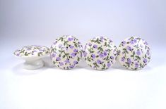 three ceramic knobs with purple flowers on them and one white knob is in the foreground