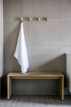 a white towel hanging on the wall next to a wooden bench in a bathroom with gray tiles