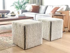 two white ottomans sitting on top of a wooden floor in front of a couch and coffee table