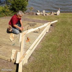 a man working on a wooden deck next to the water with ducks in the background