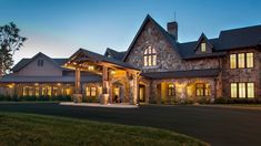 a large house with lots of windows and lights on it's front entrance at dusk