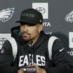 a man sitting in front of a microphone wearing a black hat and jacket with eagles on it