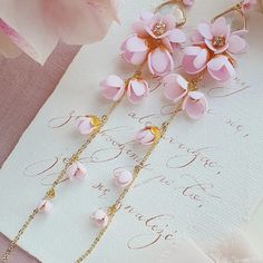 pink flowers are hanging from gold chains on top of a white paper with writing underneath