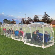 several people sitting in lawn chairs under a clear tent on the side of a soccer field