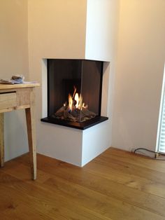 a fire is burning in a fireplace with wood flooring and a table next to it