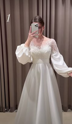 a woman taking a selfie in front of a mirror wearing a white wedding dress