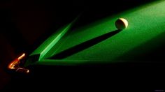 a green pool table with a white ball on it's side and the shadow of a cue