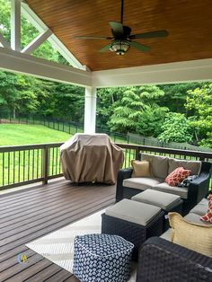 a covered deck with furniture and grill on it's side area, surrounded by lush green trees