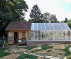 a small house with a greenhouse in the back yard, surrounded by grass and trees