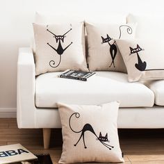 three pillows with black cats on them sitting on a white couch next to a book