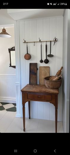 a wooden table sitting in front of a wall with hanging utensils on it