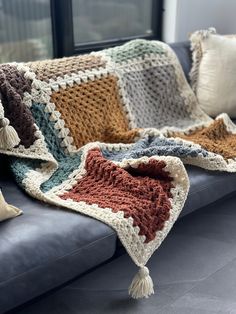 a crocheted blanket is sitting on a couch next to pillows and a pillow