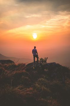 a man standing on top of a mountain with the sun setting in the sky behind him