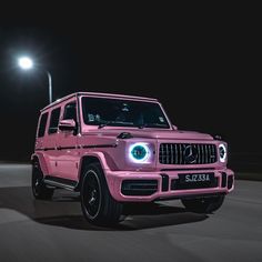 a pink mercedes g - class is driving down the road at night with its headlights on