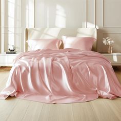 a bed with pink sheets and pillows in a white room next to a lamp on a table