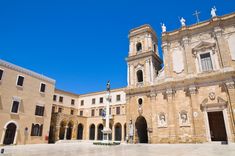 an old church with statues on the front and two story buildings in the back, against a bright blue sky