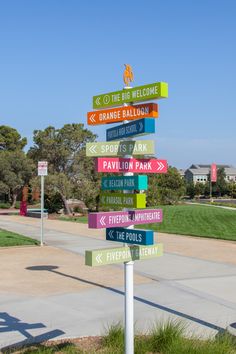 a street sign with many different colored signs on it's post in front of a park