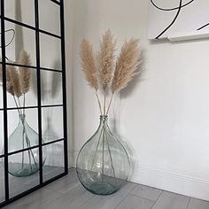 two vases with dried plants in them on a wooden floor next to a mirror