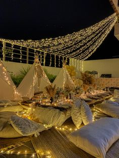 pillows and lights are on the ground in front of some teepee tents with string lights strung across them