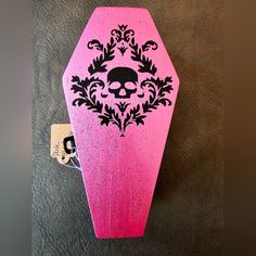 a pink skateboard with a skull and floral design on the front, sitting on a black surface