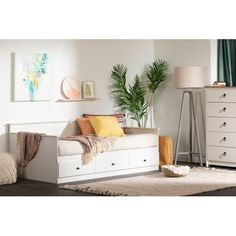 a white day bed sitting in a living room next to a dresser and lamp on top of a rug