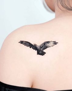 the back of a woman's shoulder with a black and white bird tattoo on it